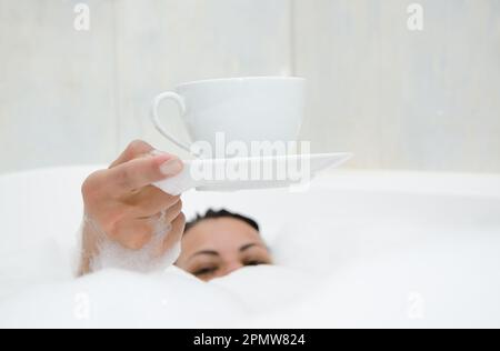 Frau trinkt einen Kaffee in der Badewanne mit Schaum. Stockfoto
