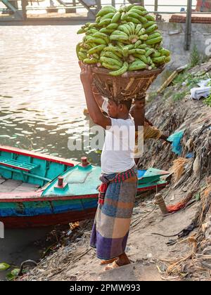 Mann mit grünen Bananen zu lokalen Fähren am Wise Ghat Boat Station am Buriganga River in Dhaka, der Hauptstadt von Bangladesch. Stockfoto