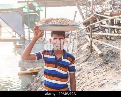 Ein Mann, der ein Tablett mit Erdnüssen zu lokalen Fähren am Wise Ghat Boat Station am Buriganga River in Dhaka, der Hauptstadt von Bangladesch, transportiert. Stockfoto