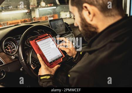 Die Hände eines Mechanikers verwenden ein Diagnosegerät zur Fehlersuche am Computersystem eines modernen Autos in einer Garage. Stockfoto