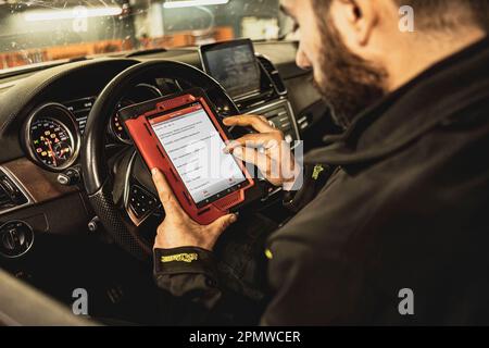 Die Hände eines Mechanikers verwenden ein Diagnosegerät zur Fehlersuche am Computersystem eines modernen Autos in einer Garage. Stockfoto