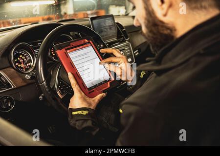 Die Hände eines Mechanikers verwenden ein Diagnosegerät zur Fehlersuche am Computersystem eines modernen Autos in einer Garage. Stockfoto