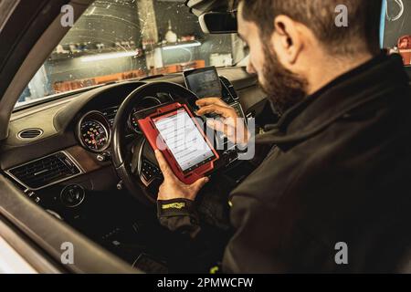 Die Hände eines Mechanikers verwenden ein Diagnosegerät zur Fehlersuche am Computersystem eines modernen Autos in einer Garage. Stockfoto
