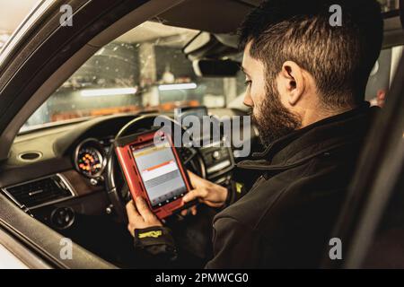 Die Hände eines Mechanikers verwenden ein Diagnosegerät zur Fehlersuche am Computersystem eines modernen Autos in einer Garage. Stockfoto