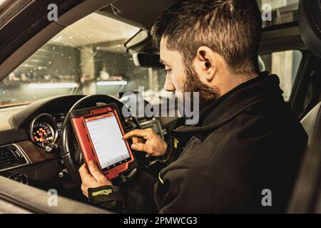 Die Hände eines Mechanikers verwenden ein Diagnosegerät zur Fehlersuche am Computersystem eines modernen Autos in einer Garage. Stockfoto