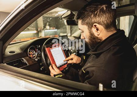 Die Hände eines Mechanikers verwenden ein Diagnosegerät zur Fehlersuche am Computersystem eines modernen Autos in einer Garage. Stockfoto