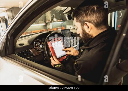 Die Hände eines Mechanikers verwenden ein Diagnosegerät zur Fehlersuche am Computersystem eines modernen Autos in einer Garage. Stockfoto