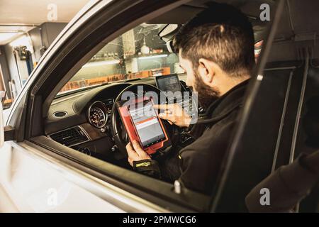 Die Hände eines Mechanikers verwenden ein Diagnosegerät zur Fehlersuche am Computersystem eines modernen Autos in einer Garage. Stockfoto
