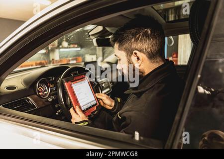 Die Hände eines Mechanikers verwenden ein Diagnosegerät zur Fehlersuche am Computersystem eines modernen Autos in einer Garage. Stockfoto