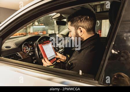 Die Hände eines Mechanikers verwenden ein Diagnosegerät zur Fehlersuche am Computersystem eines modernen Autos in einer Garage. Stockfoto