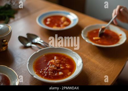 Serviertisch für Mittagessen in der Familie. Ukrainische Küche. Rote Suppe Borsch in weißen Tellern. Das Kind isst das erste Gericht mit Löffel Stockfoto