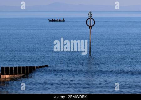 Edinburgh, Schottland, Großbritannien. 15. April 2023 Einige Aktivitäten am frühen Morgen am Strand von Portobello mit Menschen, die den milden Start in den Tag mit blauem Himmel und Sonnenschein genießen. Großes hölzernes Ruderboot in der Forth Estuary mit der hölzernen Groyne und dem Markierpfosten. Kredit: Craig Brown/Alamy Live News Stockfoto