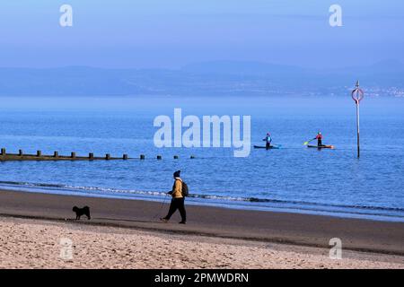 Edinburgh, Schottland, Großbritannien. 15. April 2023 Einige Aktivitäten am frühen Morgen am Strand von Portobello mit Menschen, die den milden Start in den Tag mit blauem Himmel und Sonnenschein genießen. Mit dem Hund am Strand entlang zu gehen mit Paddelboardern in der Flussmündung. Kredit: Craig Brown/Alamy Live News Stockfoto