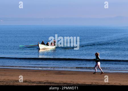 Edinburgh, Schottland, Großbritannien. 15. April 2023 Einige Aktivitäten am frühen Morgen am Strand von Portobello mit Menschen, die den milden Start in den Tag mit blauem Himmel und Sonnenschein genießen. Holzruderboot bereitet sich auf die Landung am Strand vor. Kredit: Craig Brown/Alamy Live News Stockfoto