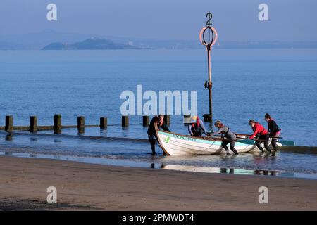 Edinburgh, Schottland, Großbritannien. 15. April 2023 Einige Aktivitäten am frühen Morgen am Strand von Portobello mit Menschen, die den milden Start in den Tag mit blauem Himmel und Sonnenschein genießen. Ein hölzernes Ruderboot ist gerade am Strand gelandet. Blick in Richtung Inchkeith. Kredit: Craig Brown/Alamy Live News Stockfoto