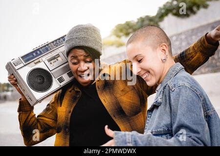 Fröhliche Multirassenmenschen tanzen zu Stadtmusik im Freien mit Stadt im Hintergrund - Frauen aus verschiedenen Kulturen feiern gemeinsam - Fokus auf afrika Stockfoto
