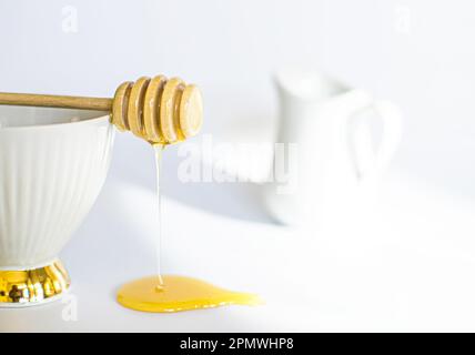 Honig fließt aus gedrehtem Honigstock. Honigs tun auf weißem Hintergrund. Frühstücksahnekännchen Stockfoto