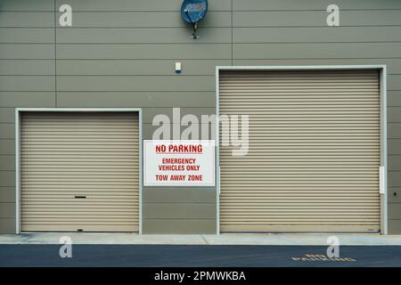 Kein Parken, nur Rettungsfahrzeuge, Abschleppzone. Grau-grüne Wand mit großen und kleinen Garagentüren. Garage für Feuerwehrwagen und Polizeifahrzeuge Stockfoto