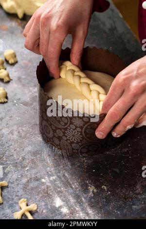 Eine Süßwarenfrau dekoriert und dekoriert traditionellen Osterkuchen mit einem aus dem Teig gewobenen Zöpfen. Osterkuchen ist ein Symbol für osterferien Stockfoto