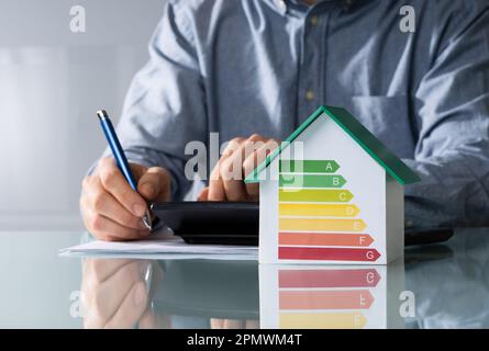 Mittelteil der Geschäftsmann Berechnung Rechnung mit energieeffizienten Diagramm auf Haus Modell im Büro Stockfoto