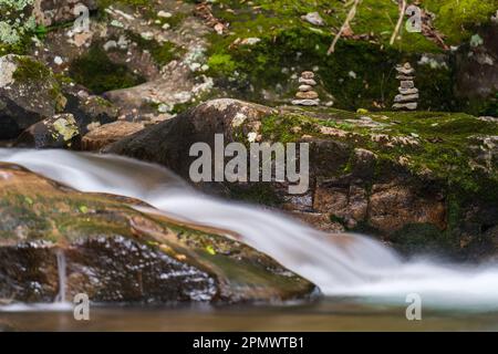 Ruhiger Fluss mit Mossy Rocks und gestapelten Steinmarkierungen Stockfoto