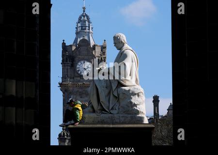 Edinburgh, Schottland, Großbritannien. 15. April 2023 Sonniger und klarer blauer Himmel über der Stadt und den East Princes Street Gardens mit abenteuerlustigen Kindern, die über das Walter Scott Monument und die Statue klettern. Kredit: Craig Brown/Alamy Live News Stockfoto