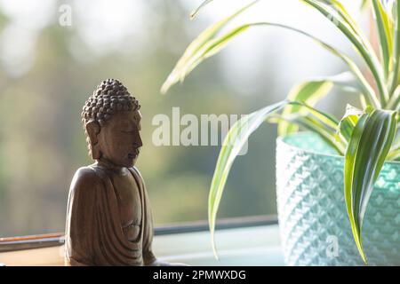 Hölzernes Bild von Buddha auf dem Fenster neben dem Blumentopf, Nahaufnahme Stockfoto