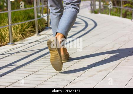 Die Füße des Fußgängers Geschäftsmann. Ein Mann in grauen Hosen, braune Schuhe, der an sonnigen Tagen auf der großen Straße spaziert. Lifestyle-Konzept für Geschäfts- und Urlaubsreisen. Contrasti Stockfoto