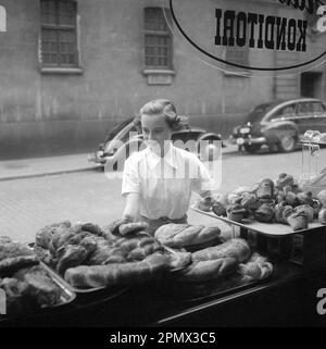 In den 1950er Jahren. Eine Frau wird auf der Straße und an der Ladenfront einer Bäckerei abgebildet. Sie sieht aus, als ob sie sich entscheidet, was sie kaufen möchte, und sieht von der guten Auswahl an süßem Brot und Brötchen verlockt aus. Schweden 1951 Kristoffersson Ref BD91-5 Stockfoto