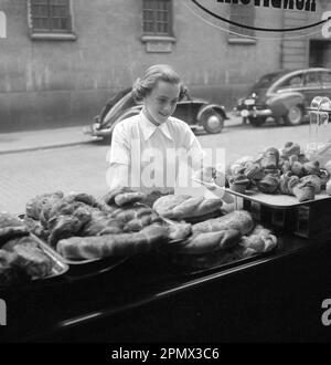 In den 1950er Jahren. Eine Frau wird auf der Straße und an der Ladenfront einer Bäckerei abgebildet. Sie sieht aus, als ob sie sich entscheidet, was sie kaufen möchte, und sieht von der guten Auswahl an süßem Brot und Brötchen verlockt aus. Schweden 1951 Kristoffersson Ref BD91-4 Stockfoto