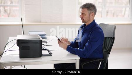 Geschäftsmann, Der Im Büro Druckbefehle Auf Einem Smartphone Ausgibt Stockfoto