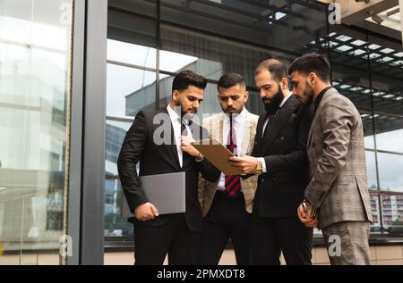 Ein internationales Team erfolgreicher junger Geschäftsleute in Anzügen diskutiert bei einem Treffen gemeinsam die Umsetzung von Businessplänen. Stockfoto