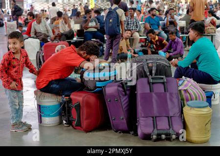 Ein verspielter indischer Junge, der seinen schlafenden Vater ärgert, ihre Familie am Chhatrapati Shivaji Maharaj Terminus in Mumbai, Indien, und auf ihren Zug wartet Stockfoto