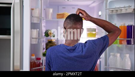 Rückansicht eines verwirrten jungen Mann auf der Suche nach Essen im Kühlschrank Stockfoto