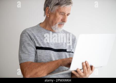 Ein älterer Mann, der zu Hause einen Laptop benutzt, ein bisschen mit der Technologie zu kämpfen hat, während der COVID-Sperre/Quarantäne online einkaufen Stockfoto