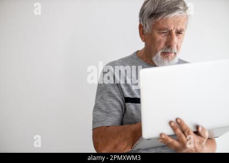 Ein älterer Mann, der zu Hause einen Laptop benutzt, ein bisschen mit der Technologie zu kämpfen hat, während der COVID-Sperre/Quarantäne online einkaufen Stockfoto