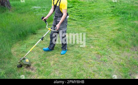 Ein männlicher Gärtner mäht das grüne Gras des Rasens im Garten mit einem Benzinmäher. Trimmer für die Pflege eines Gartengrundes Stockfoto