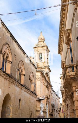 Mdina, Malta - 13. November 2022: Straße mit Kalksteingebäuden und Karmelitenkirche, auch bekannt als Verkündigungskirche mit Glockenspiel und Jungfrau Stockfoto