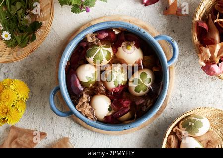 Ostereier mit frischen Kräutern werden mit Zwiebelschalen in einem blauen Topf gefärbt, Draufsicht Stockfoto