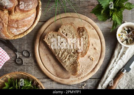 Sauerteigbrot mit frischen essbaren Wildpflanzen - gemahlener älterer, stechender Nesselnessel und Gänseblümchen Stockfoto