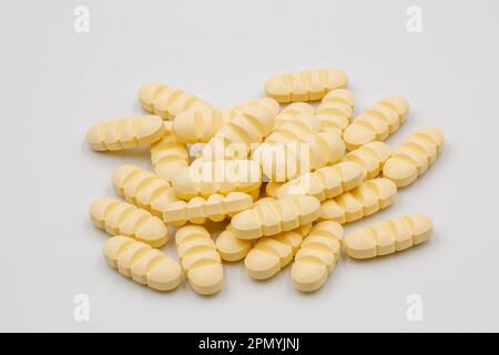 Ein Stapel gelber länglicher Tabletten mit Teilstreifen zur Aufteilung in vier Teile, Nahaufnahme auf weiß. Stockfoto