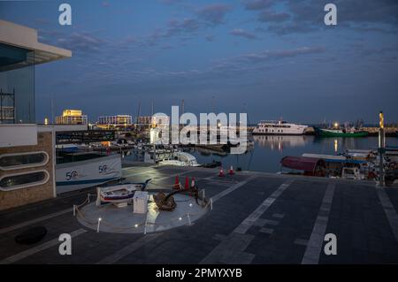 Limassol, Zypern - 23. März 2023 - Blick über den alten Hafen in der Abenddämmerung mit reflektierenden Booten, Gebäuden und bunten Nachtlichtern Stockfoto