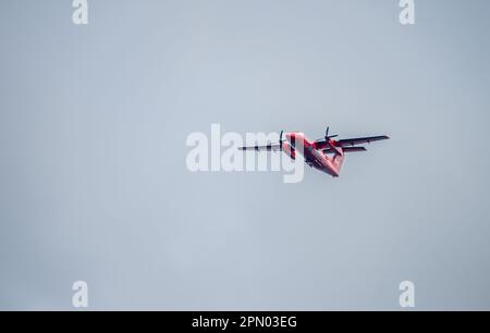 Ein rotes Transport Canada Aerial Dash-8 Turboprop NASP Überwachungsflugzeug fliegt an einem bedeckten Tag über uns. Stockfoto