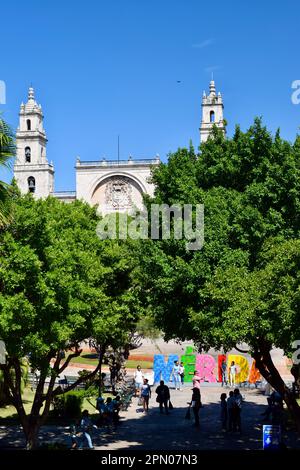 Die Kathedrale von Merida, auch bekannt als Kathedrale von San Ildefonso, vom Stadtpalast aus gesehen, mit Touristen, die sich am Merida-Schild auf der Plaza Grande posieren. Stockfoto