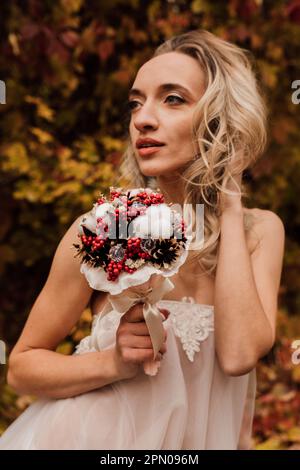 Schöne Braut mit einem Blumenstrauß in der Hand. Hochzeit im Herbst im Wald Stockfoto