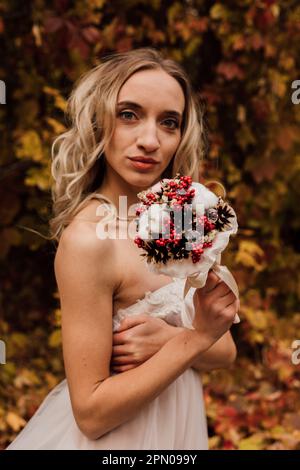 Schöne Braut mit einem Blumenstrauß in der Hand. Hochzeit im Herbst im Wald Stockfoto