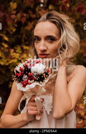 Schöne Braut mit einem Blumenstrauß in der Hand. Hochzeit im Herbst im Wald Stockfoto