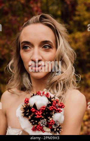 Schöne Braut mit einem Blumenstrauß in der Hand. Hochzeit im Herbst im Wald Stockfoto