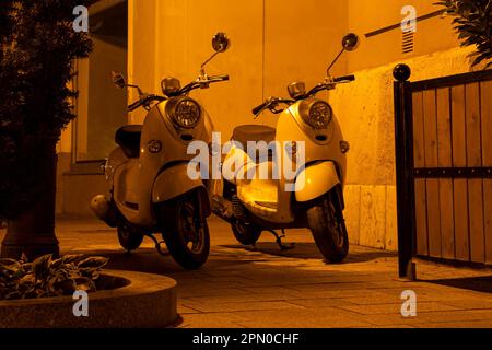 Zwei klassische Retro-Roller in gelblicher Lampenbeleuchtung auf der Straße Stockfoto
