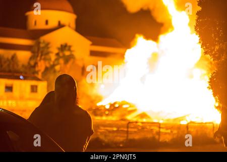 Limassol, Zypern. 15. April 2023. Ein Paar beobachtet das große Feuer namens "Lampratzia", das vor einer Kirche brennt und soll das Böse in Limassol, Zypern, am 15. April 2023 verbannen. Orthodoxe Christen feiern die Auferstehung Jesu Christi mit einer Zeremonie, die um Mitternacht stattfindet, am Wechsel vom Heiligen Samstag zum Ostersonntag. (Foto: Kostas Pikoulas/Sipa USA) Kredit: SIPA USA/Alamy Live News Stockfoto